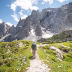 Randonneur sur un sentier d’altitude en été, face à des sommets rocheux enneigés