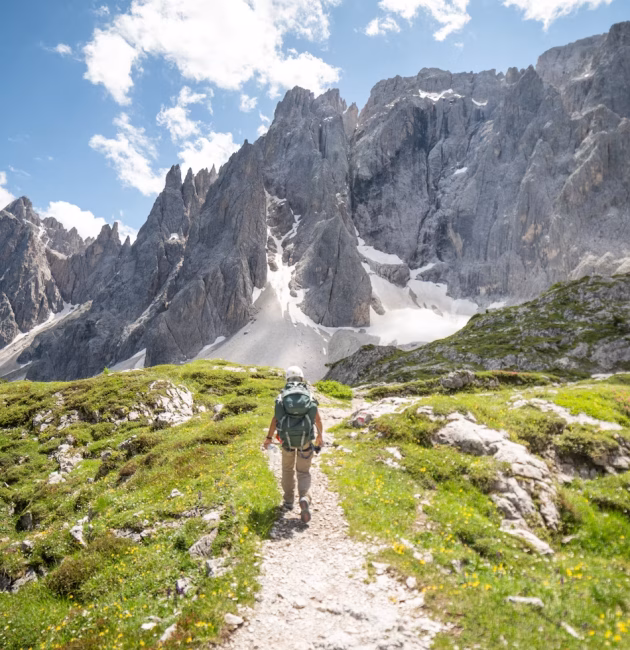 Randonneur sur un sentier d’altitude en été, face à des sommets rocheux enneigés