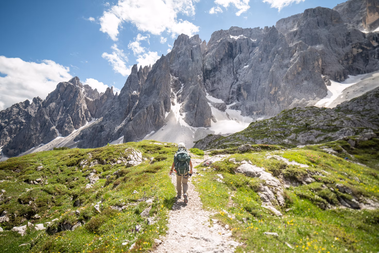 Randonneur sur un sentier d’altitude en été, face à des sommets rocheux enneigés
